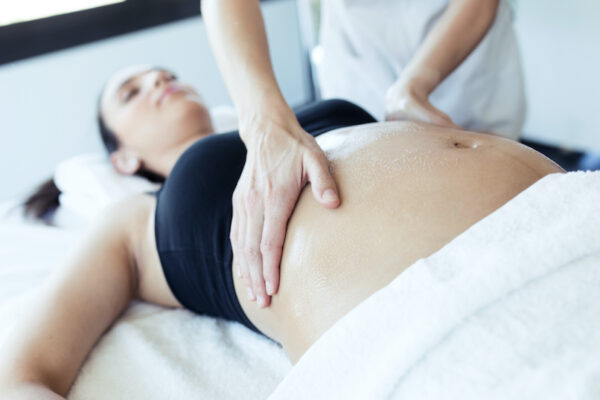 Close-up of female physiotherapist massaging tummy on pregnant woman in spa center.